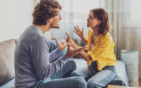 Un couple en plein conflit dans le salon, leurs visages tendus et leurs mains agitées témoignent d'une dispute animée.