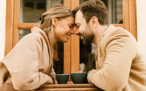 Un couple partage un moment intime, leurs fronts se touchant, illustrant l'effet miroir en amour. Deux tasses de café attendent sur la table.
