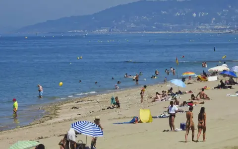 Plage bondée, baigneurs dans l'eau bleue. Combien de temps avant d'aller chez lui ? La journée s'étire.