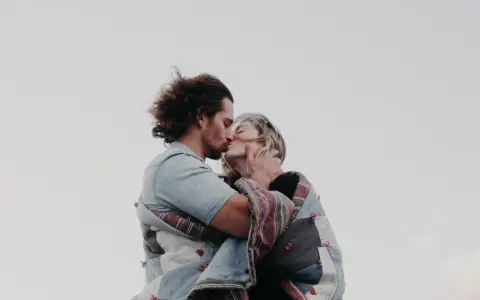 Un couple s'embrasse tendrement, enveloppé dans une couverture. Une belle illustration de comment trouver un mec et vivre un amour sincère.