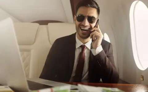 Un homme d'affaires souriant, lunettes de soleil, au téléphone dans un jet privé. Il semble rencontrer un homme riche pour conclure un accord.