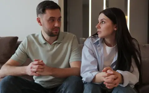 Un couple, peut-être un peu psycho, se regarde intensément, les mains jointes, sur un canapé.