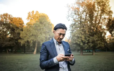 Un homme en costume, concentré sur son téléphone, dans un parc automnal. Une phrase provocante pour un homme pourrait être écrite sur son écran.