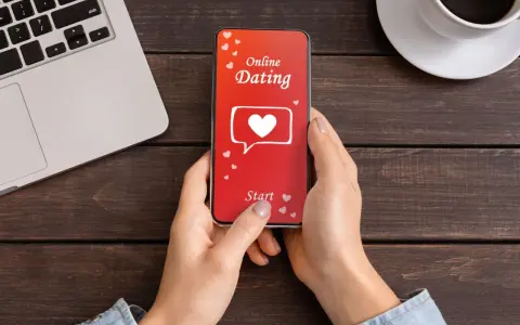 Une personne utilise une appli de rencontre sur son téléphone. L'écran affiche "Online Dating" avec un cœur.