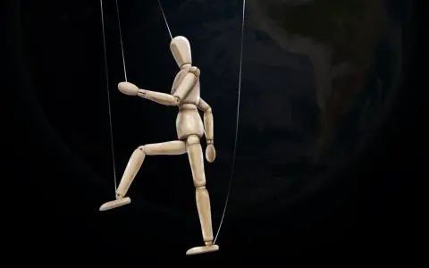 Marionnette de bois suspendue par des fils, se faisant désirer devant la Terre.