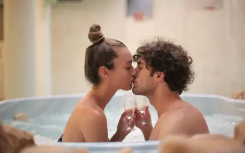 Un couple s'embrasse tendrement dans un jacuzzi, deux coupes de champagne à la main, pour un bain romantique inoubliable.