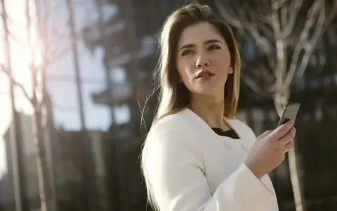 Une femme en manteau blanc tient un téléphone, prête à challenger un homme par sms.