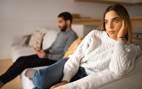 Un couple s'ennuie dans son couple, chacun absorbé par son téléphone sur le canapé, le regard perdu dans le vide.