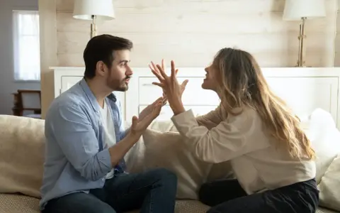 Un couple se dispute sur un canapé. L'homme semble frustré, peut-être parce qu'il est jaloux.