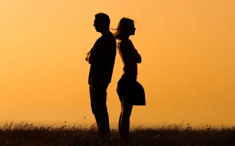 Silhouettes d'un homme et d'une femme dos à dos, bras croisés, symbolisant la communication paradoxale dans un paysage au coucher du soleil.