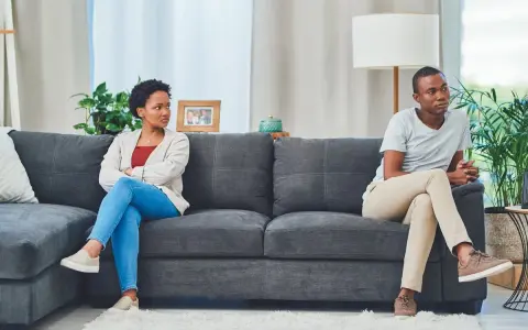 Un couple assis sur un canapé, dos à dos, l'air distant. Elle, les bras croisés, le regarde avec une expression de lassitude. Il, pensif, détourne le regard. Je l'aime mais je ne le supporte plus.