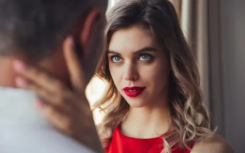 Un homme regarde intensément une femme aux yeux bleus et aux lèvres rouges, vêtue d'une robe rouge.