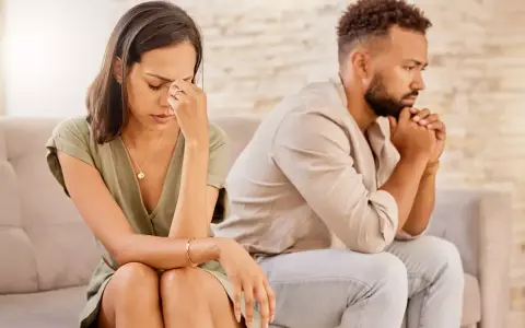 Un couple assis dos à dos, visiblement affecté par des disputes incessantes. La femme se tient la tête, l'air accablé, tandis que l'homme fixe le vide, les mains jointes.