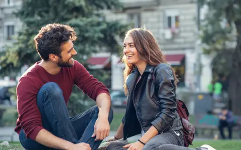Un homme qui veut vous voir, assis sur l'herbe, rit avec une jeune femme. Ils semblent partager un moment complice et joyeux.