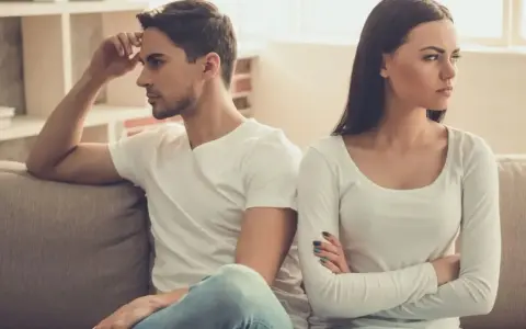 Un couple assis sur un canapé, dos à dos, visiblement en conflit. Elle croise les bras, l'air contrarié, comme s'il la prenait pour acquise.
