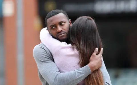 Un homme étreint une femme, mais son regard trahit des signes qu'il parle à une autre.