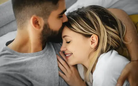 Un homme embrasse le front d'une femme endormie, un moment de tendresse calin amoureux.