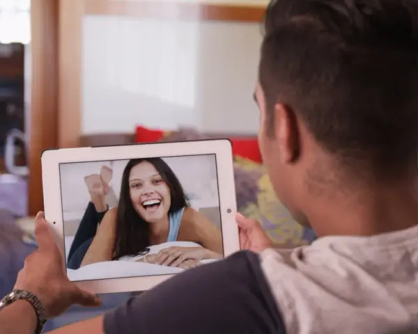 Un homme en relation à distance profite d'un appel vidéo avec sa compagne, dont le sourire illumine l'écran de sa tablette.
