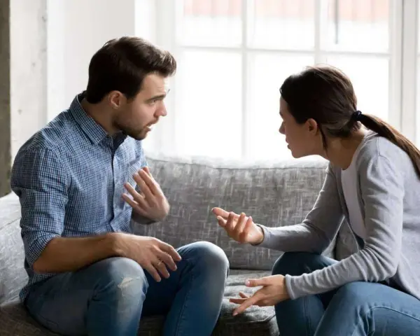 Un couple discute sur un canapé, les mains tendues, peut-être lors d'une séance de thérapie de couple pour améliorer leur communication.