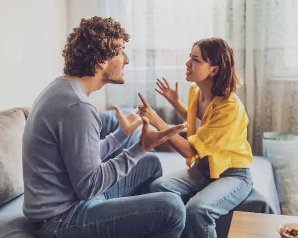 Un couple en plein conflit dans le salon, leurs visages tendus et leurs mains agitées témoignent d'une dispute animée.