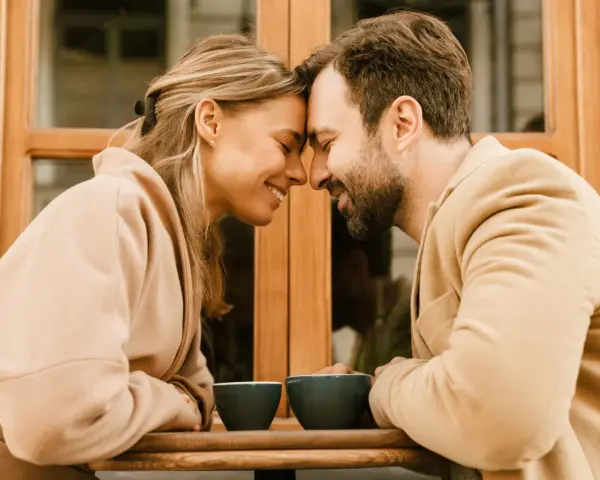 Un couple partage un moment intime, leurs fronts se touchant, illustrant l'effet miroir en amour. Deux tasses de café attendent sur la table.
