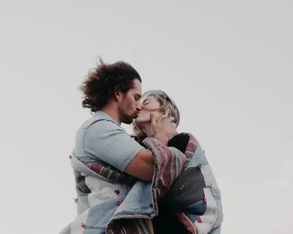 Un couple s'embrasse tendrement, enveloppé dans une couverture. Une belle illustration de comment trouver un mec et vivre un amour sincère.