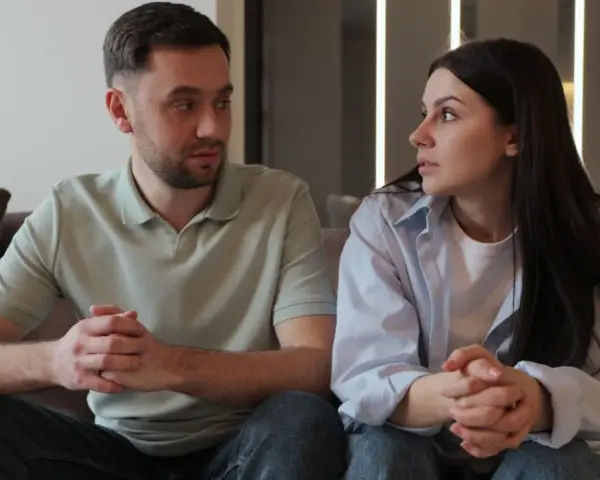 Un couple, peut-être un peu psycho, se regarde intensément, les mains jointes, sur un canapé.
