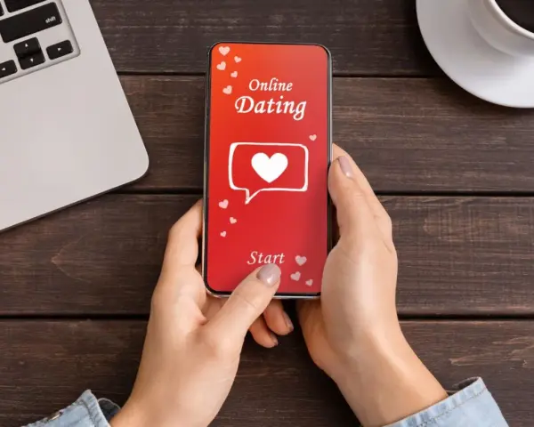 Une personne utilise une appli de rencontre sur son téléphone. L'écran affiche "Online Dating" avec un cœur.