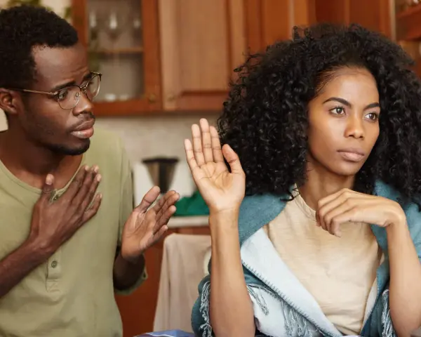 Un homme avec des lunettes parle avec passion, la main sur le cœur, tandis que sa femme, le regard ailleurs, lève une main en signe d'arrêt. Il dit : "je ne supporte plus ma femme.