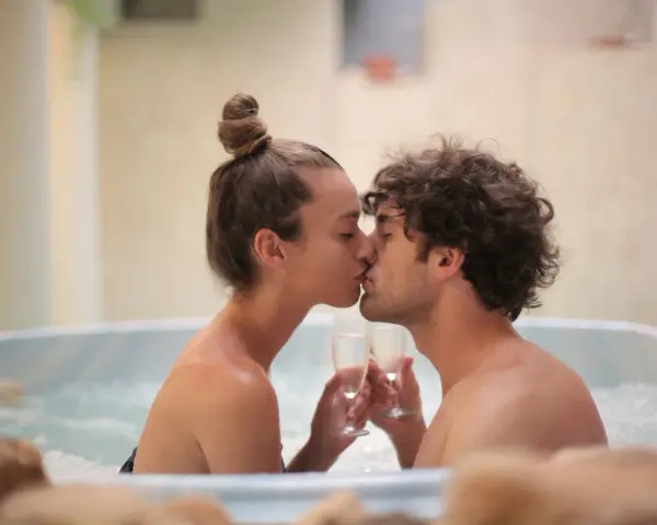 Un couple s'embrasse tendrement dans un jacuzzi, deux coupes de champagne à la main, pour un bain romantique inoubliable.
