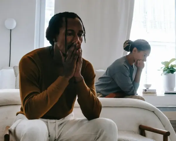 Un couple traverse une crise, visiblement préoccupés, assis séparément dans une chambre lumineuse.