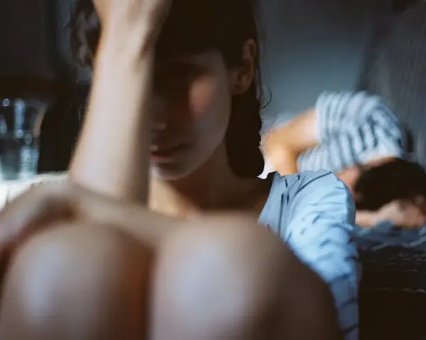 Une femme au premier plan, le visage caché, semble accablée. Au fond, une autre personne se recroqueville. L'image évoque la **dépression et la libido** affectées par le mal-être.