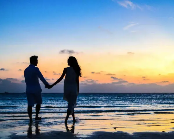 Silhouettes d'un couple se tenant la main sur une plage au coucher du soleil. Il tient à moi mais n'est pas amoureux, juste un ami.