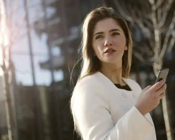 Une femme en manteau blanc tient un téléphone, prête à challenger un homme par sms.