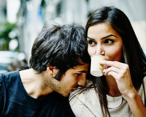 Un homme murmure à l'oreille d'une femme qui boit son café. Un tendre début de relation, peut-être le surnom qu'il vient de lui donner.