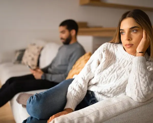 Un couple s'ennuie dans son couple, chacun absorbé par son téléphone sur le canapé, le regard perdu dans le vide.