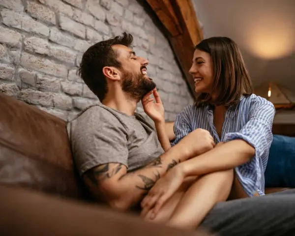 Un couple rit et se regarde tendrement sur un canapé. Le vrai amour, c'est cette complicité.