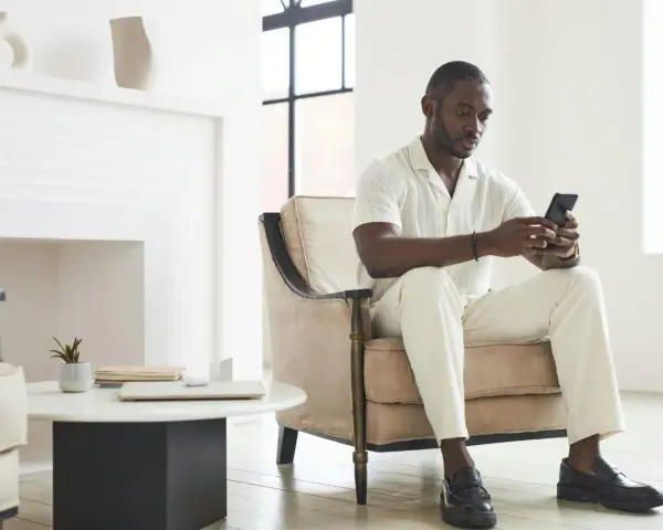 Un homme en tenue claire, assis dans un fauteuil, regarde son téléphone. Il attend un message, car il ne m'écrit plus comme avant.