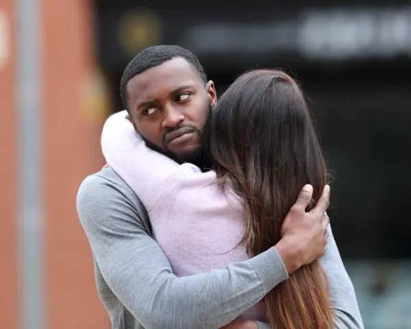 Un homme étreint une femme, mais son regard trahit des signes qu'il parle à une autre.