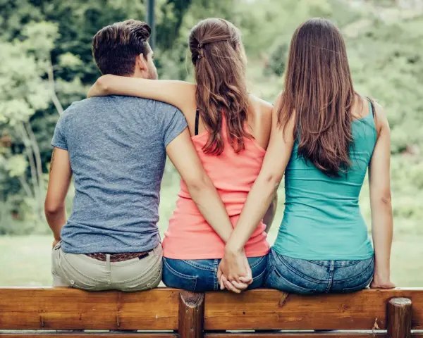 Trois personnes assises sur un banc, un homme entre deux femmes. Les mains des femmes se serrent derrière le dos de l'homme. Je ne le trouve pas beau mais il m'attire.