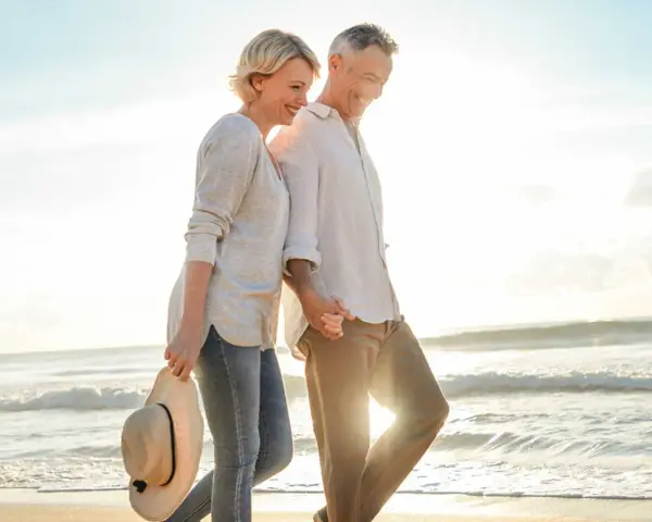 Un couple profite d'un rendez-vous amoureux sur la plage, main dans la main, au coucher du soleil.