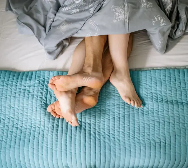 Pieds entrelacés sous une couette, évoquant la chaleur et la libido femme.