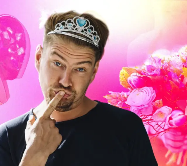 Un homme porte une tiare de princesse, un doigt sur les lèvres, à côté d'une boîte en forme de cœur et d'un bouquet de fleurs roses.