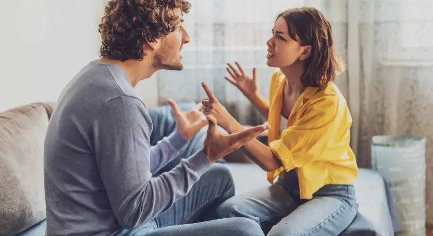 Un couple en plein conflit dans le salon, leurs visages tendus et leurs mains agitées témoignent d'une dispute animée.