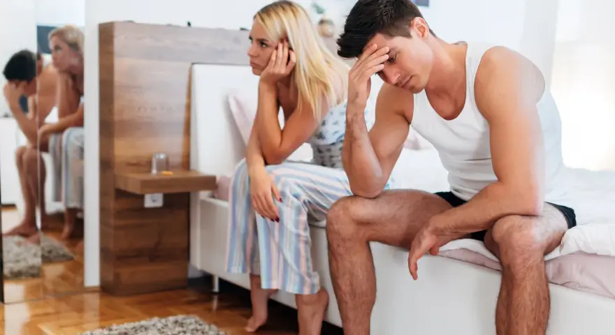 Couple assis sur un lit, l'air préoccupé. L'homme, la quarantaine, se tient la tête, son **libido homme 45 ans** peut-être en question.