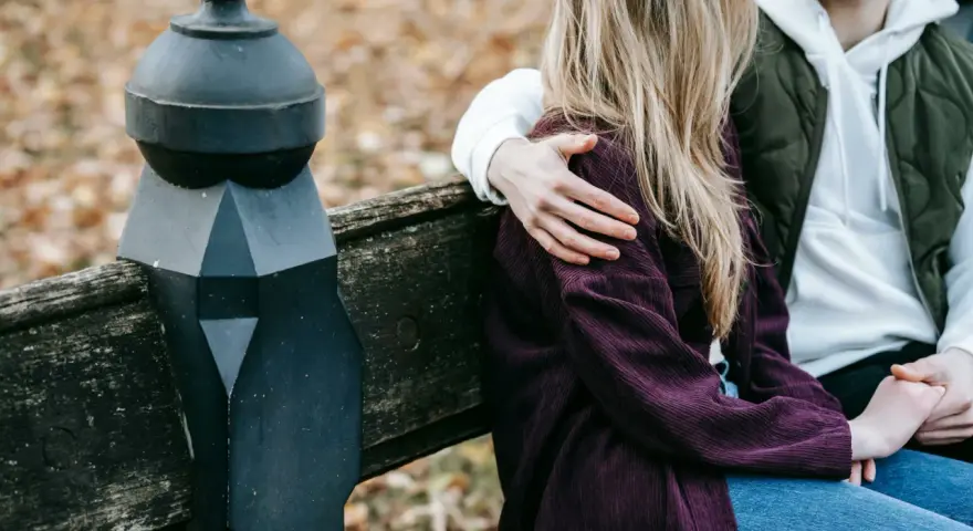 Un homme enlace tendrement une femme assise à ses côtés sur un banc. Un geste qui dit "comment dire je t'aime sans le dire".
