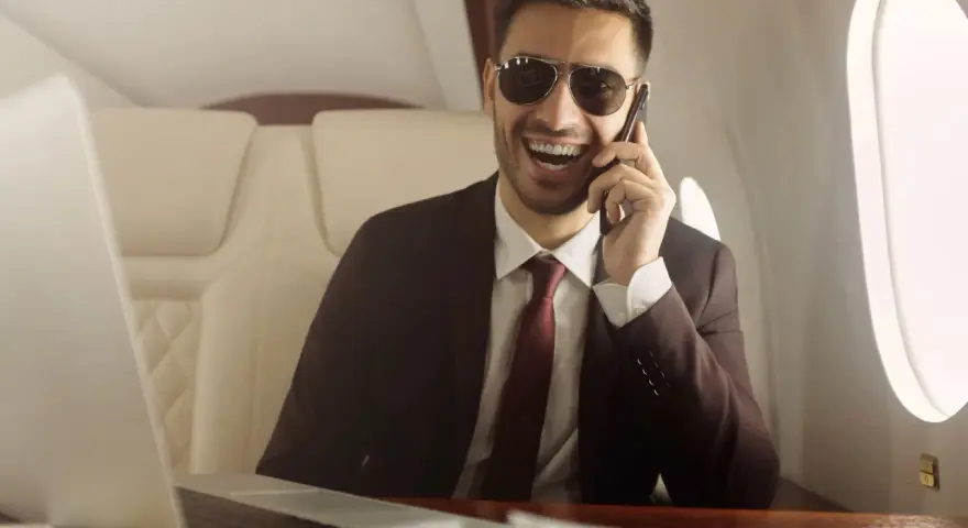 Un homme d'affaires souriant, lunettes de soleil, au téléphone dans un jet privé. Il semble rencontrer un homme riche pour conclure un accord.