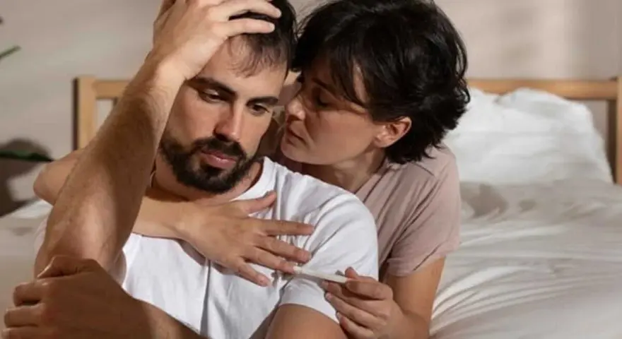 Une femme réconforte son mari, visiblement bouleversé, tenant un test de grossesse. Mon mari n'est pas affectueux, mais il est là pour moi.