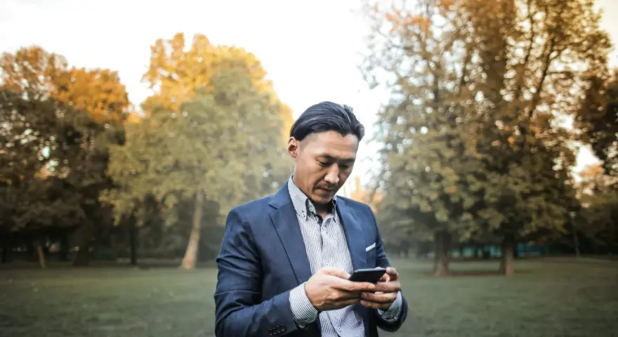 Un homme en costume, concentré sur son téléphone, dans un parc automnal. Une phrase provocante pour un homme pourrait être écrite sur son écran.