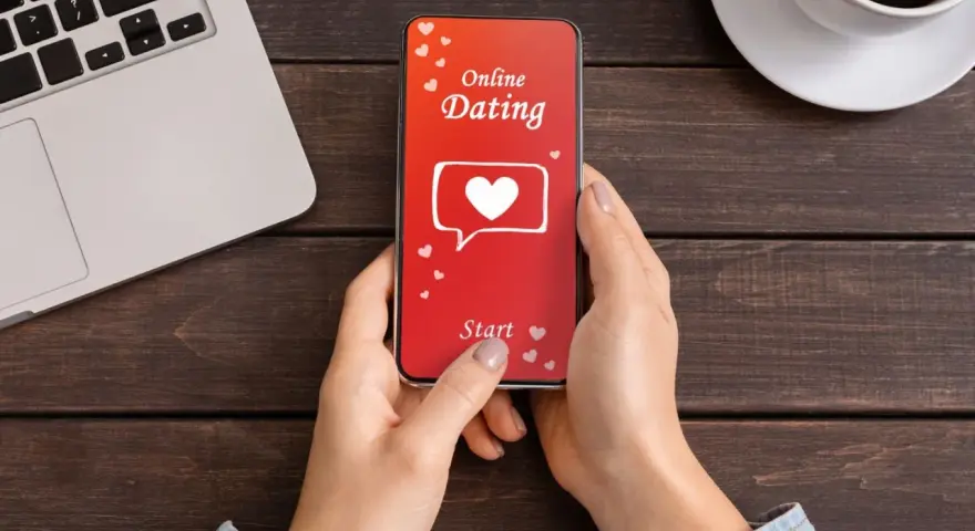 Une personne utilise une appli de rencontre sur son téléphone. L'écran affiche "Online Dating" avec un cœur.
